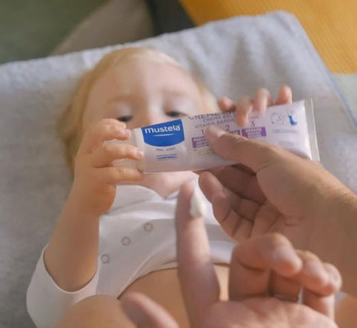 Bébé qui tient dans ses mains la crème change Mustela - Mustela Benelux - 1