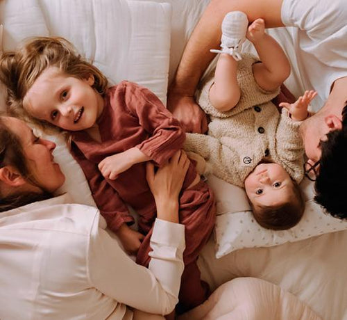 Deux parents allongés sur un lit avec leurs deux filles - Mustela Benelux - 1