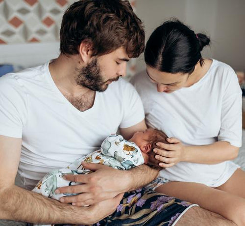 Couple assis regardant leur nouveau-né dans leurs bras - Mustela Belgium - 1