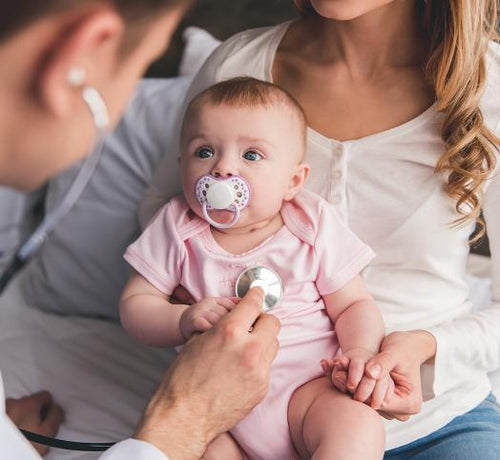 Bébé fille assis sur les genoux de sa maman pedant q'un docteur ausculte le bébé - Mustela Belgium - 1