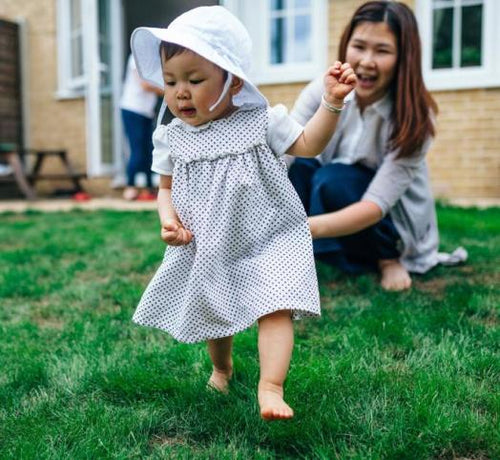 Enfant fille avec une robe et un chapeau blanc marchant dans l'herbe - Mustela Benelux - 1