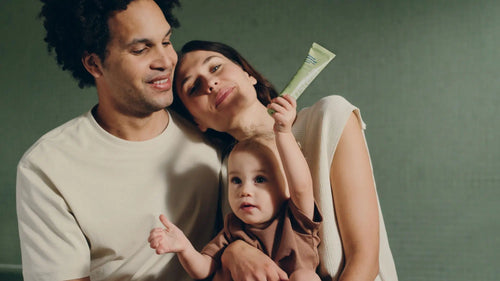 Une famille, composée d'une maman, d'un papa et d'un enfant au milieu tenu dans les bras de sa maman, avec à la main Mustela Famille Baume Universel Avocat Nourrissant - Mustela Benelux - 6