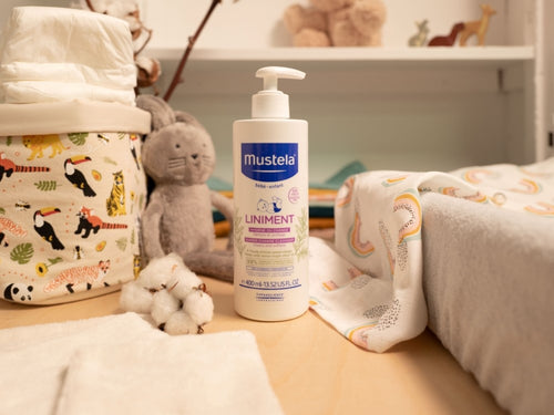 Liniment Mustela pour bébé posé sur une table à langer à côté de produits pour bébé tels que couches et vêtements. - Mustela Benelux - 3