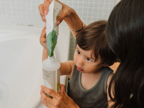 Une maman remplissant le flacon Mustela Famille Gel Lavant Bio Recharge 400ml avec l'aide de son petit garçon dans une salle de bain - Mustela Benelux - 2